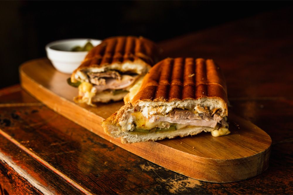 https://d4donline.com/blog/content/images/2022/03/traditional-cuban-sandwich-with-cheese-ham-fried-pork-served-wooden-board.jpg