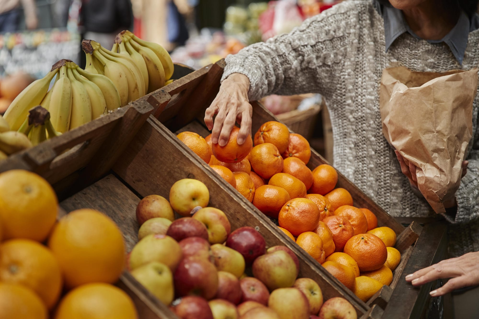 A woman is reaching into a box to pick fresh fruit, showcasing her selection process.