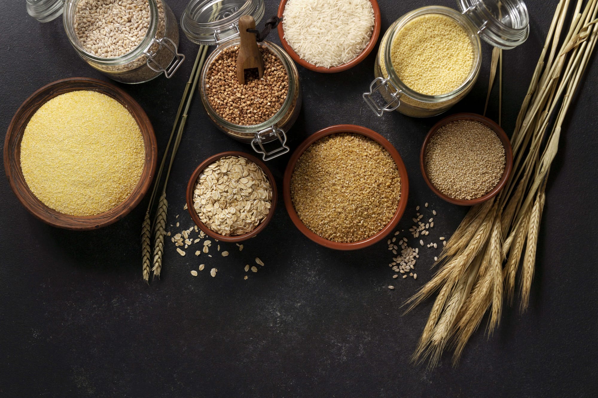 Different types of grains arranged in bowls on a black background, highlighting their diversity and natural hues.