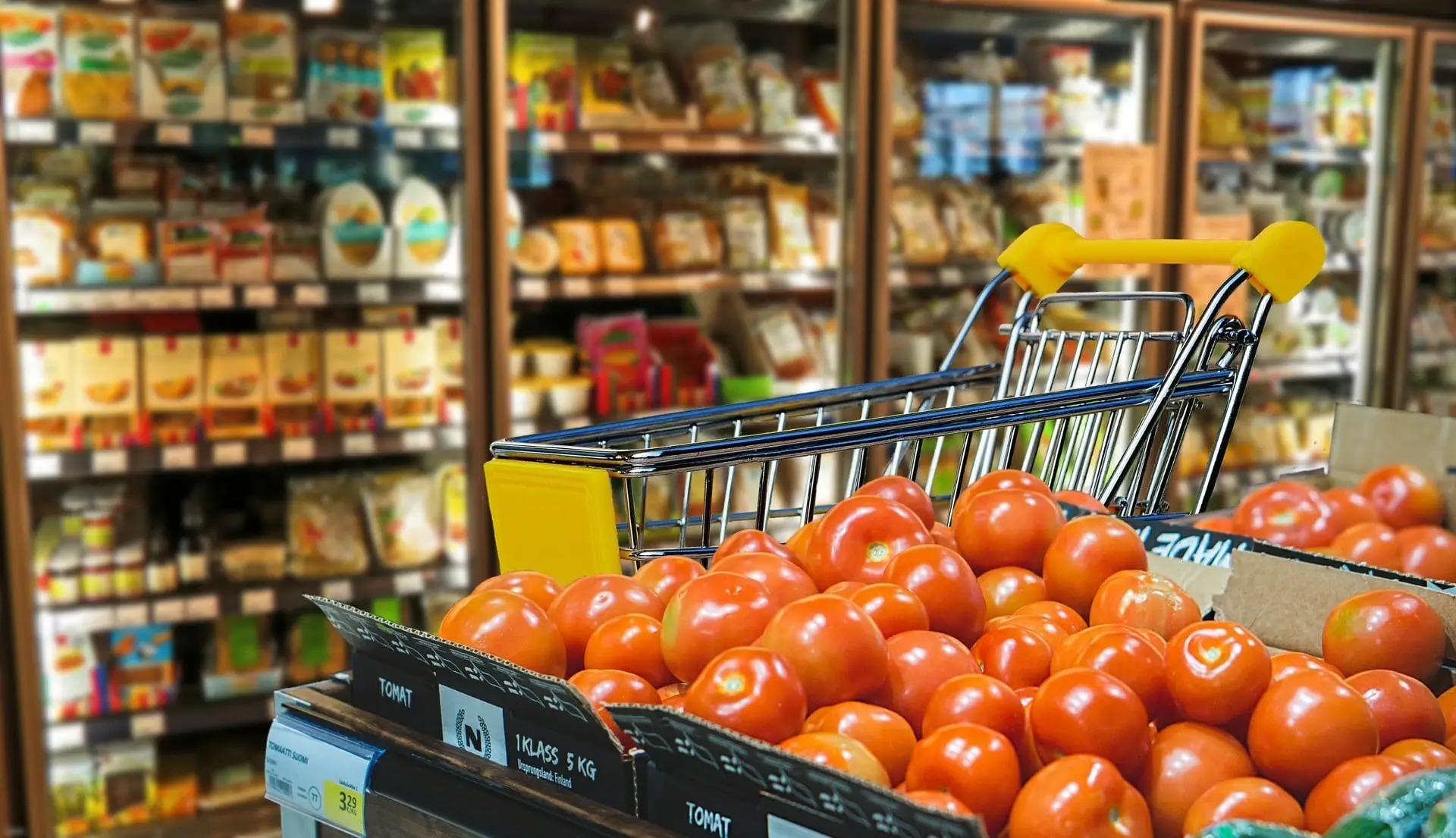 Box of tomatoes next to a refrigerator in a supermarket.