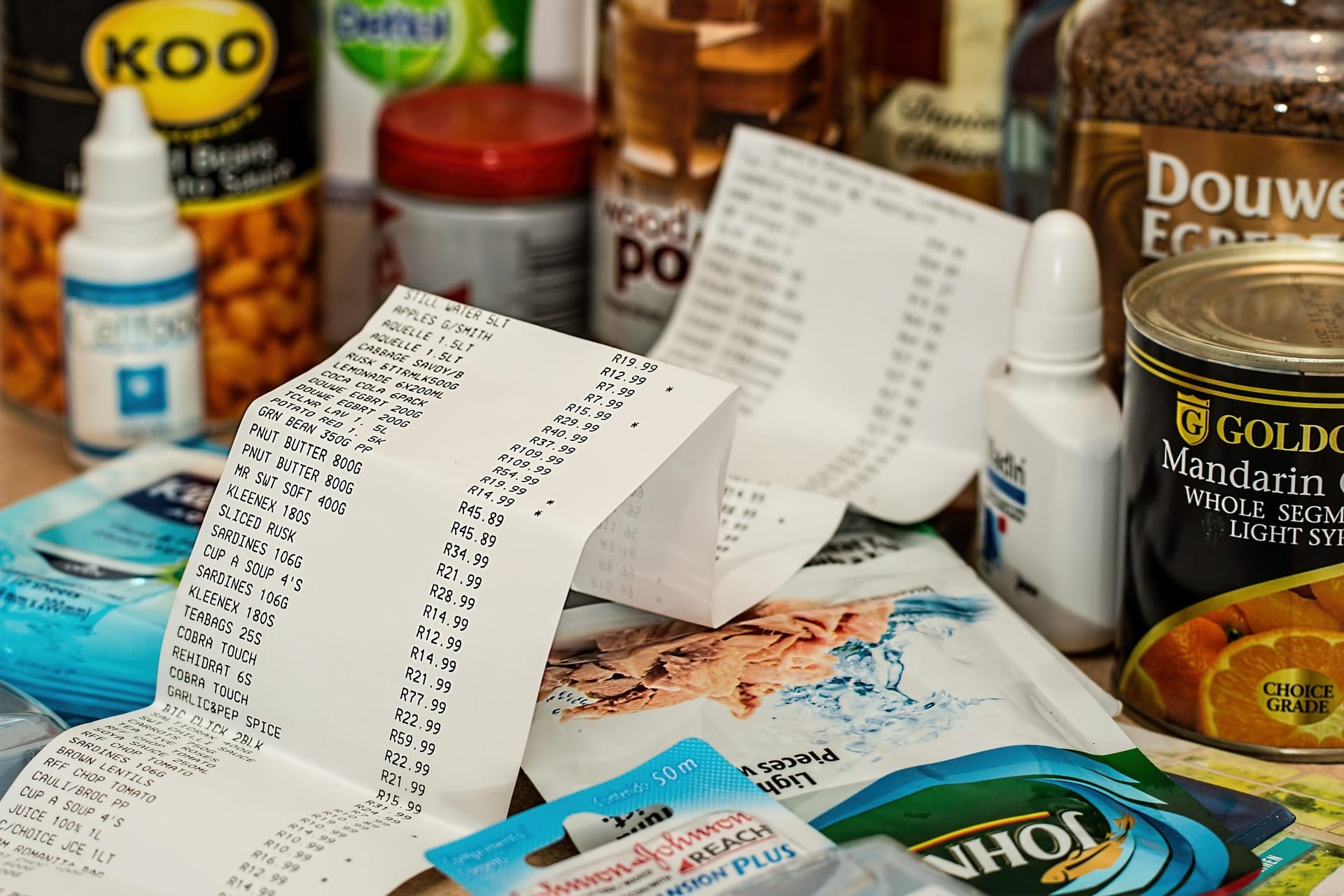 Grocery receipt surrounded by canned goods, medicine drops, and household essentials.