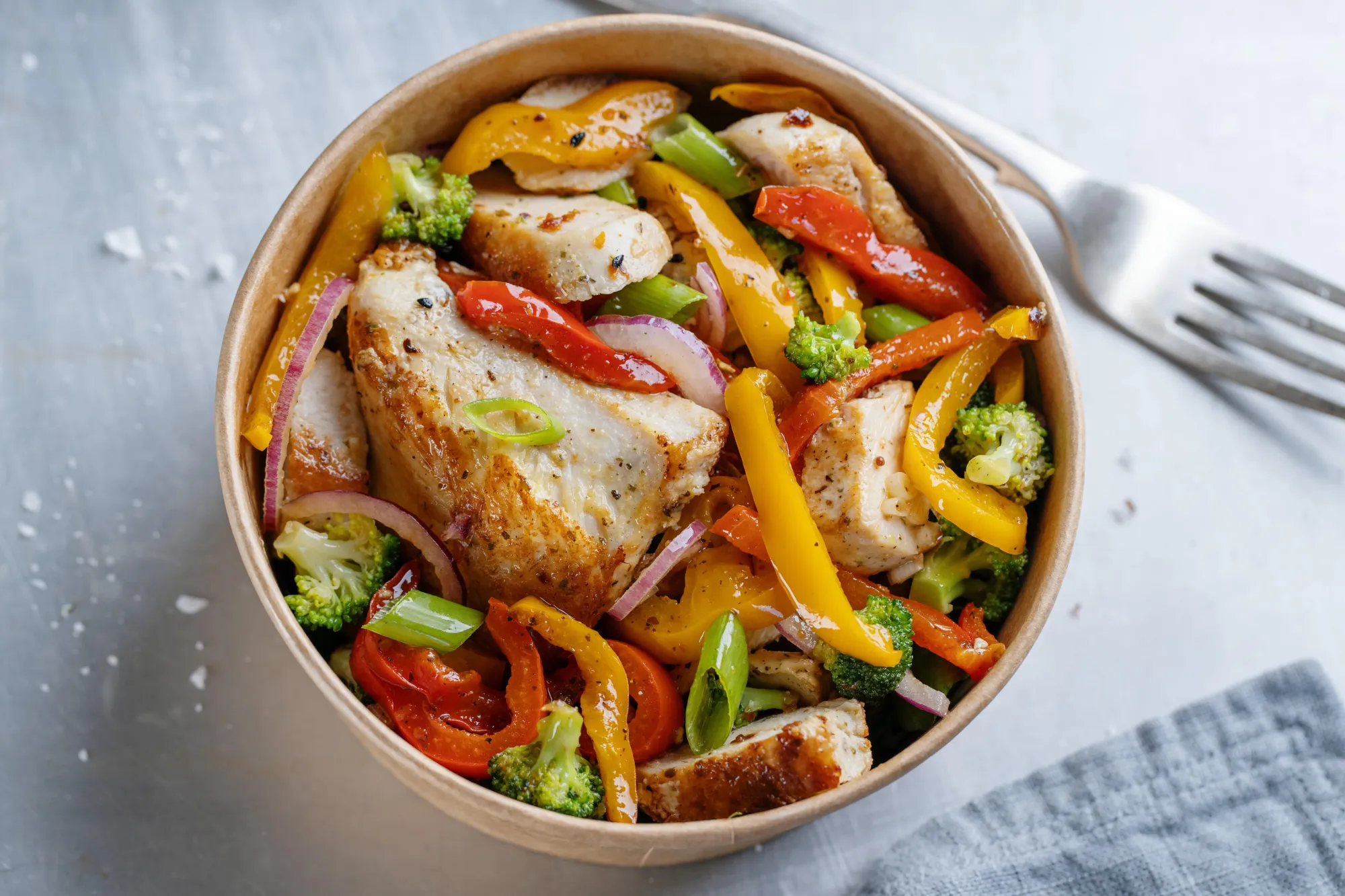 A bowl with skinless chicken breast, vegetables and broccoli.