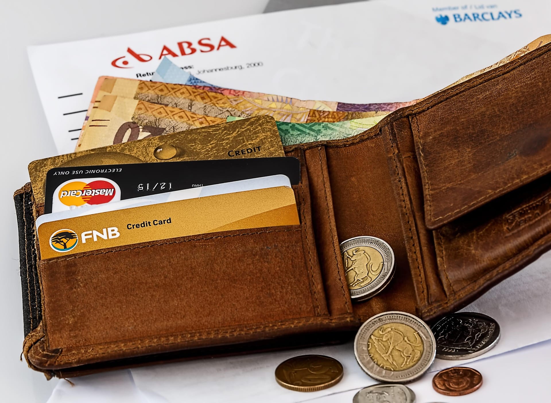Open brown leather wallet displaying credit cards, paper currency, and few coins.