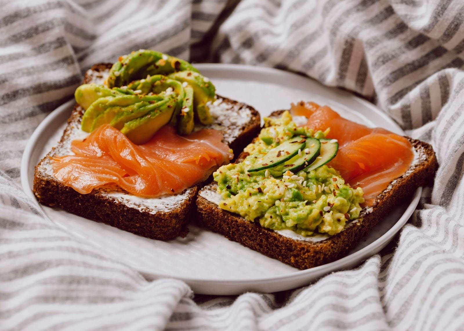 A plate consisting of tuna, avocado, cucumber slices and two breads.