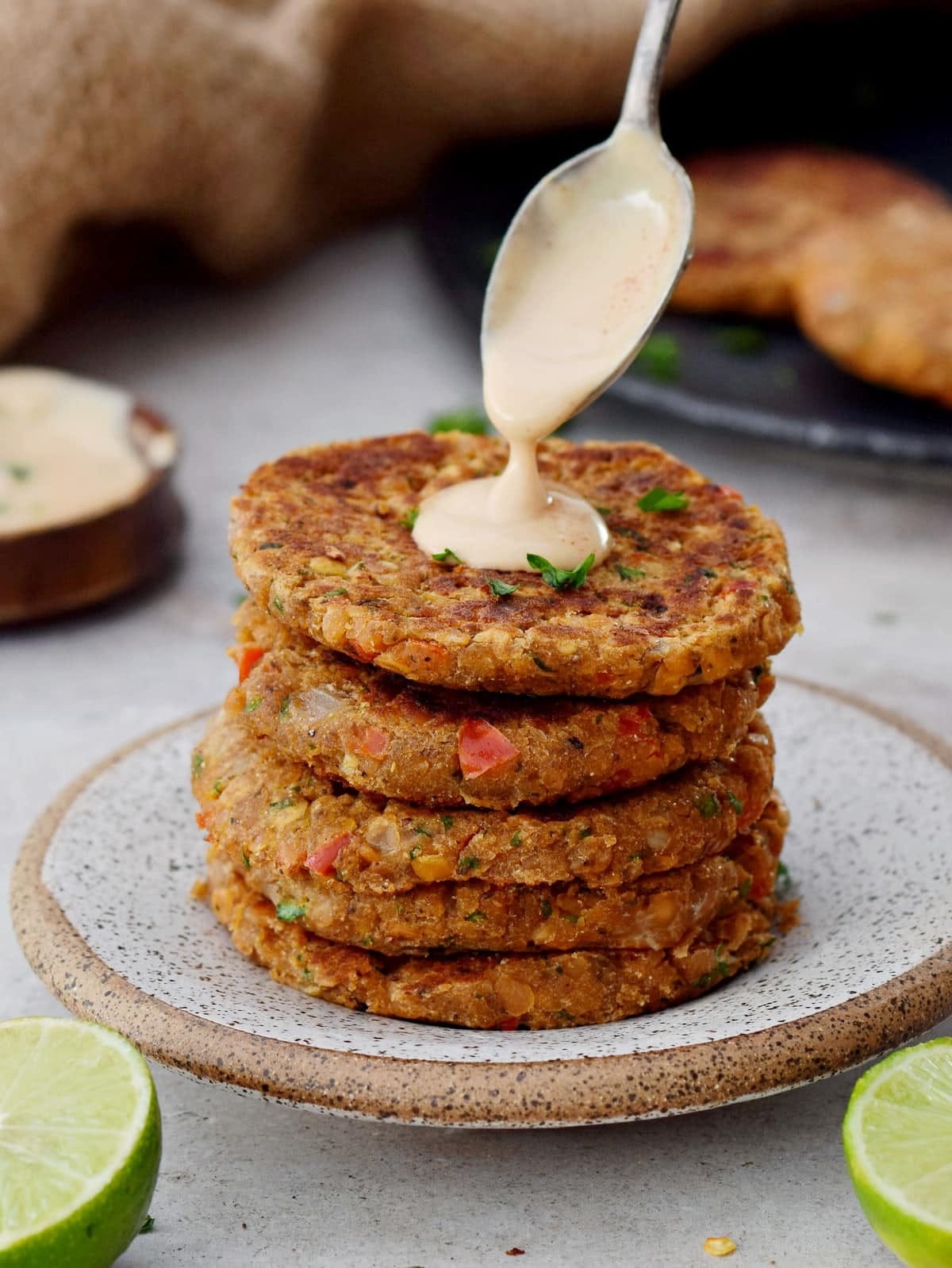 https://elavegan.com/wp-content/uploads/2021/02/stack-of-lentil-patties-with-spoon-drizzling-creamy-white-sauce-on-top.jpg